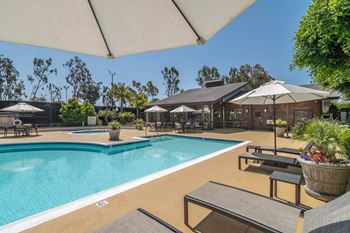 a swimming pool with tables and umbrellas and a building in the background